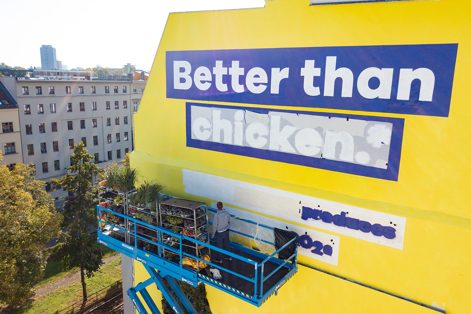 Close-up of the ‘Better than chicken.*’ lettering on the yellow wall with a scissor lift in front